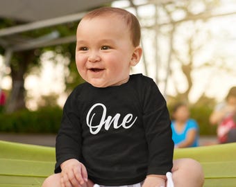 Camiseta infantil de manga comprida para o primeiro aniversário, com estampa "ONE" em cursiva. Ideal para presentear em festas, comemorações ou para celebrar o aniversário de um ano de idade.