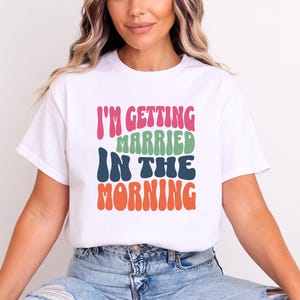 May include: White t-shirt with the text "I'm getting married in the morning" in colourful retro font.