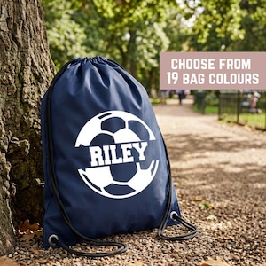 May include: A navy blue drawstring bag featuring a white graphic of a soccer ball with the name RILEY printed in the center. The bag has black cord straps and a rectangular text overlay stating CHOOSE FROM 19 BAG COLOURS in white letters.
