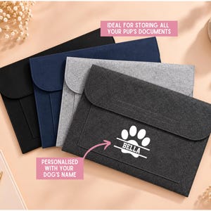 May include: A set of four rectangular felt document folders in black, navy blue, light grey, and dark grey. The dark grey folder features a white graphic of a paw print with the name BELLA printed inside, and text reading IDEAL FOR STORING ALL YOUR PUP'S DOCUMENTS and PERSONALISED WITH YOUR DOG'S NAME.