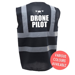 Puede incluir: Chaleco de seguridad negro con rayas reflectantes y el texto "DRONE PILOT" en blanco. Un icono de dron está por encima del texto. El chaleco está disponible en varios colores.