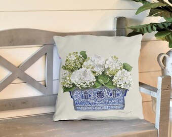 May include: A white throw pillow with a blue and white porcelain planter with white hydrangeas. The pillow has the text "Old Blue Garden" printed on the bottom.