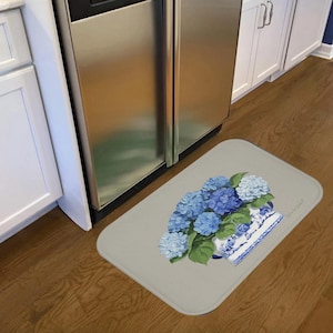Puede incluir: Una alfombra de cocina gris con un diseño floral azul y blanco. El diseño presenta un ramo de hortensias azules en un jarrón de cerámica blanco con un patrón azul y blanco. El jarrón está sentado sobre un fondo gris.