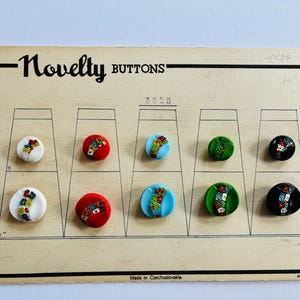 May include: A vintage card of novelty buttons. The card is beige with the words "Novelty Buttons" printed in black. The buttons are round and feature colourful floral designs. The card reads "Made in Czechoslovakia".