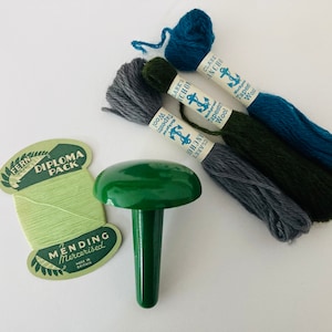 May include: A green plastic thimble with a sharp point, used for needlework.  Three balls of yarn are included: teal, grey, and forest green.  The yarn labels read "Clarke's Anchor Tapestry Wool".  A small card reads "Fern Diploma Pack Mending Mercerised Made in England".
