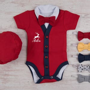 May include: A red short-sleeved bodysuit with a white collar, a red bow tie, and a dark blue button placket featuring four red buttons. The chest displays a white graphic of a leaping deer above the name Aiden. Includes a red cap and five bow ties.