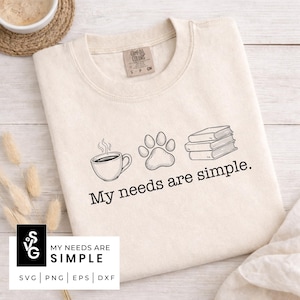 May include: Cream-colored sweatshirt with a graphic of a coffee cup, paw print, and books. The text "My needs are simple" is printed below the graphics. The sweatshirt has a crew neck and a tag that says "Comfort Colors".