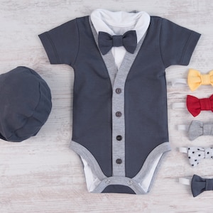 May include: A dark gray baby onesie with a gray and white cardigan-style design and a black bow tie. The onesie has short sleeves and a white collar. There are five different bow ties on a white background.