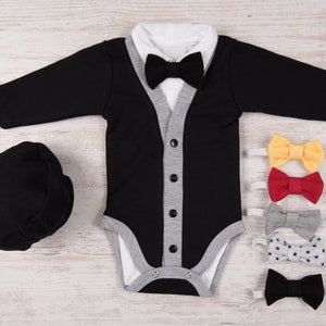 May include: A black and grey baby outfit with a white collar and a black bow tie. The outfit is paired with a black hat and four bow ties in different colors and patterns.