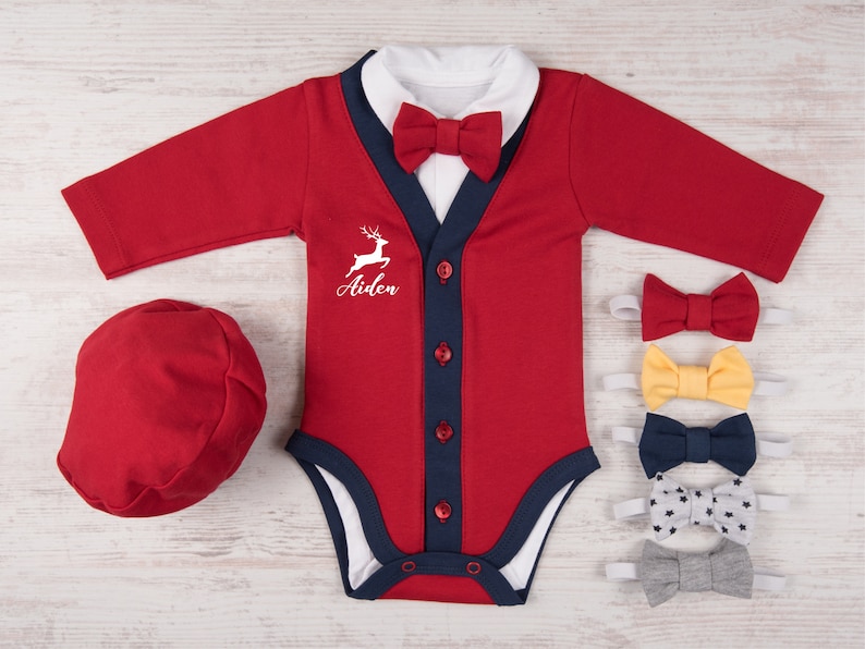 Puede incluir: Un body rojo de manga larga con cuello blanco, tapeta azul marino con cuatro botones rojos y pajarita roja a juego. El pecho presenta un gr&aacute;fico blanco de un ciervo saltando y el nombre Aiden. Incluye una gorra roja y cinco pajaritas extra.