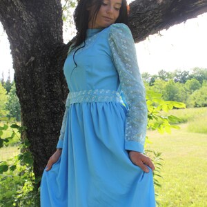 May include: A woman wearing a light blue dress with white lace sleeves and a white lace trim around the waist. The dress has a full skirt and is knee-length.