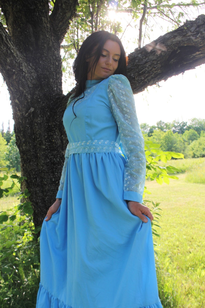 May include: A woman wearing a light blue dress with white lace sleeves and a white lace trim around the waist. The dress has a full skirt and is knee-length.