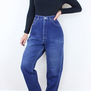 May include: A person wearing a black turtleneck shirt and high-waisted blue denim jeans. The jeans have a straight leg and are cuffed at the bottom. The person is wearing black shoes.