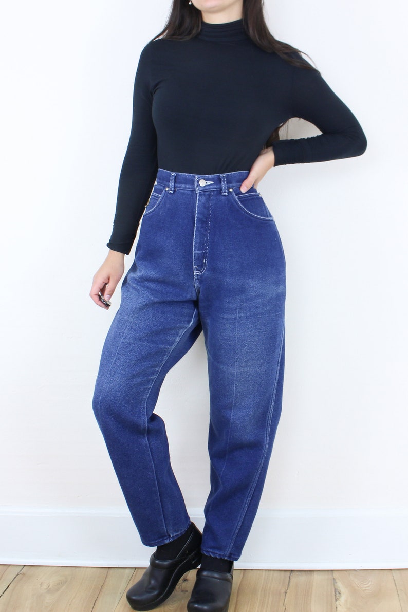 May include: A person wearing a black turtleneck shirt and high-waisted blue denim jeans. The jeans have a straight leg and are cuffed at the bottom. The person is wearing black shoes.