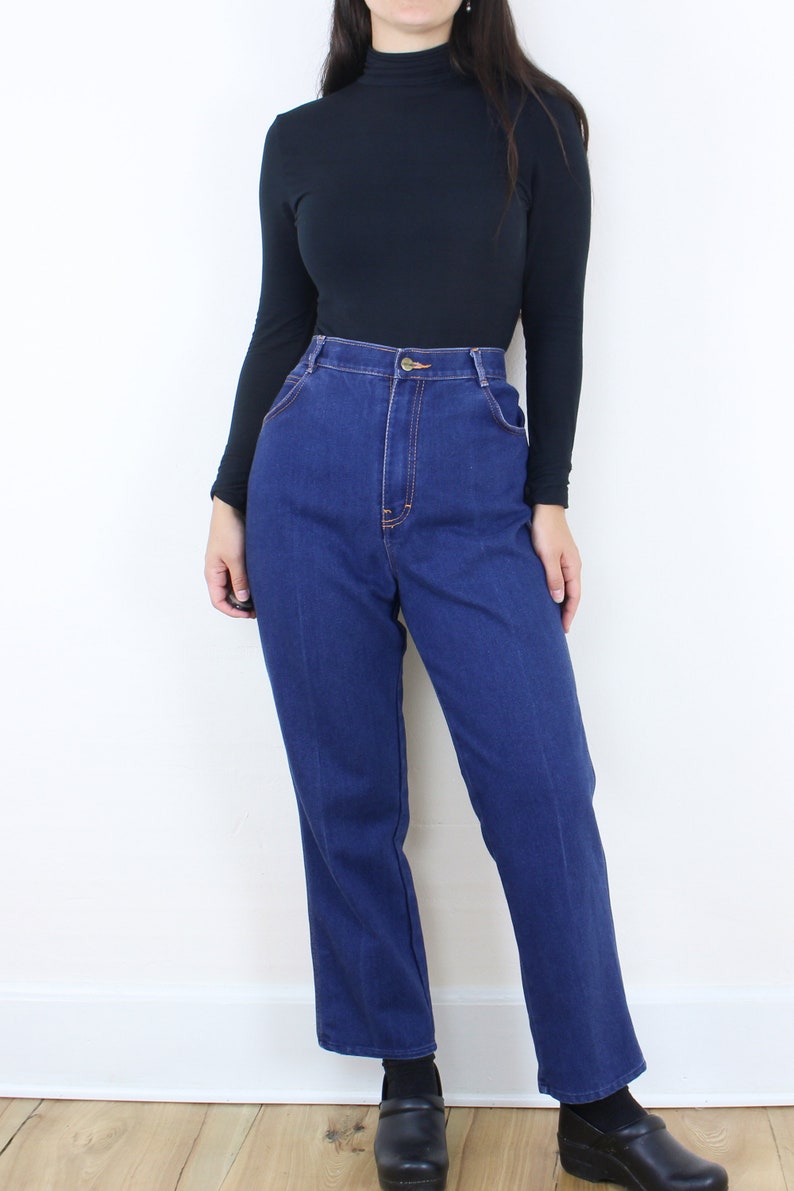 May include: A person wearing a black turtleneck shirt and blue high-waisted jeans. The jeans have a straight leg and are a dark blue wash.