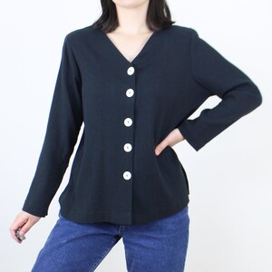 May include: A black long-sleeved button-up shirt with a v-neck and white buttons.