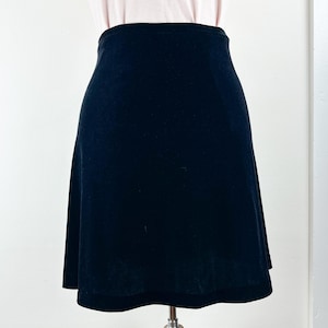May include: A black, knee-length skirt with a slight A-line shape. The skirt is made of a soft, velvety material and has a simple, classic design. The skirt is displayed on a mannequin.