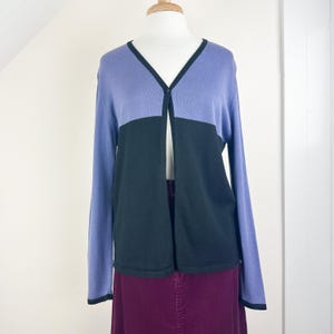 May include: A long-sleeved cardigan with a v-neck and a single button closure. The cardigan is a two-tone design with a purple top and a black bottom.