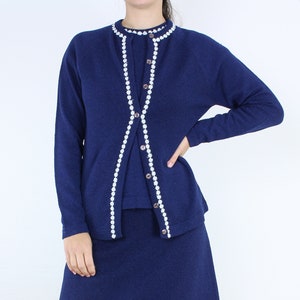 May include: A navy blue cardigan sweater with a white pearl trim. The cardigan has a button closure and a matching skirt.