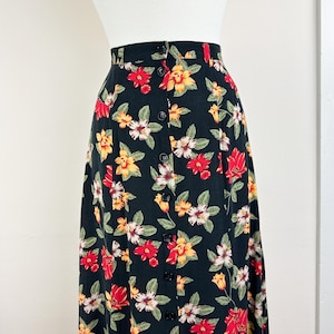 May include: A black midi skirt with a floral print featuring red, yellow, and white flowers. The skirt has a button-up front closure.