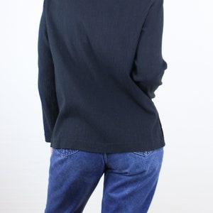 May include: A dark blue long-sleeved shirt with a relaxed fit. The shirt is made of a soft, textured fabric. The model is wearing the shirt with blue jeans.