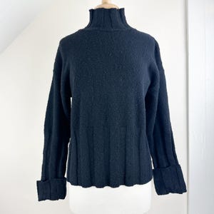 May include: A black turtleneck sweater with long sleeves and a ribbed texture. The sweater has a slightly cropped length and cuffed sleeves.