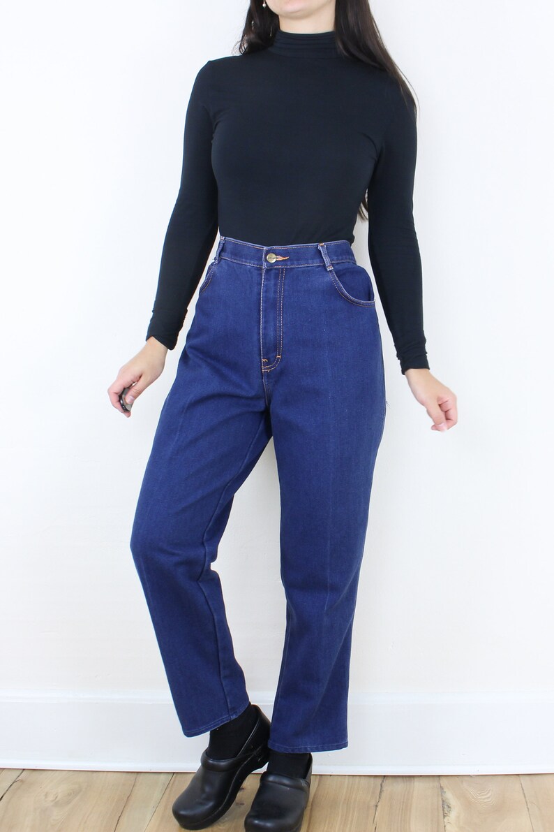 May include: A person wearing a black turtleneck shirt and blue high-waisted jeans. The jeans have a straight leg and are a dark wash.
