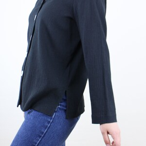 May include: A black long-sleeved button-up shirt with a v-neckline. The shirt is made of a textured fabric and has a slightly loose fit.