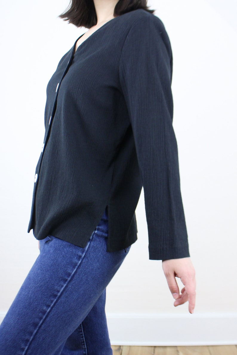 May include: A black long-sleeved button-up shirt with a v-neckline. The shirt is made of a textured fabric and has a slightly loose fit.