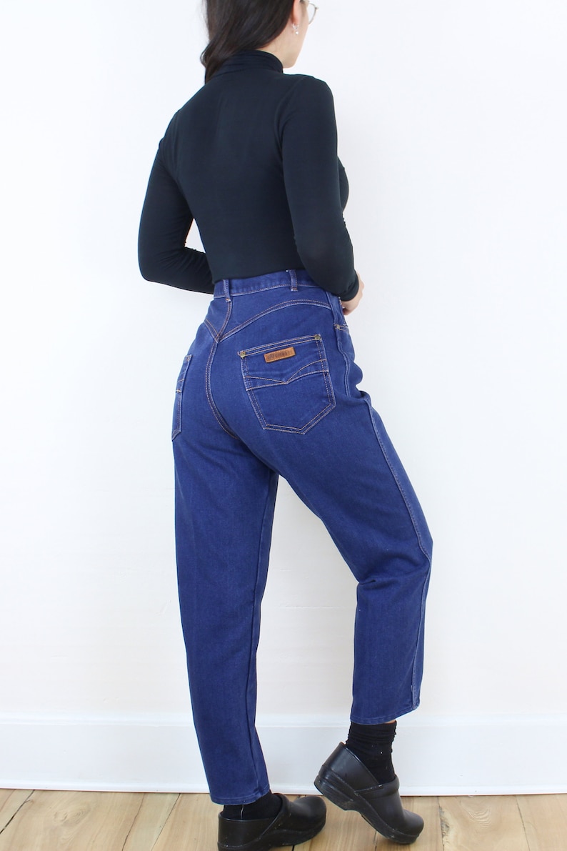 May include: A pair of high-waisted blue denim jeans with a brown leather patch on the back pocket.