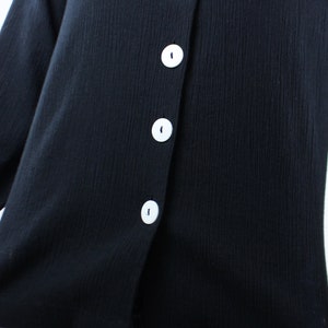 May include: A black button-up shirt with white buttons. The shirt is made of a soft, textured fabric.