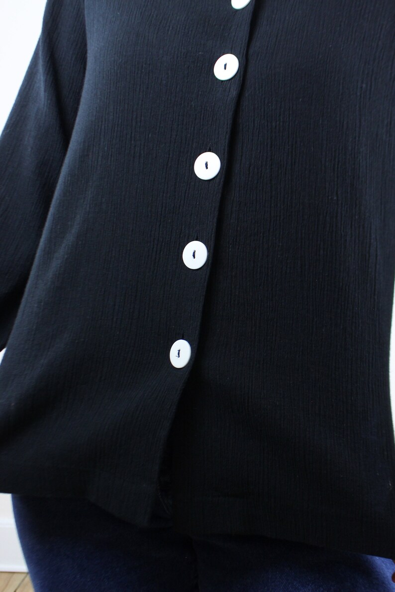 May include: A black button-up shirt with white buttons. The shirt is made of a soft, textured fabric.
