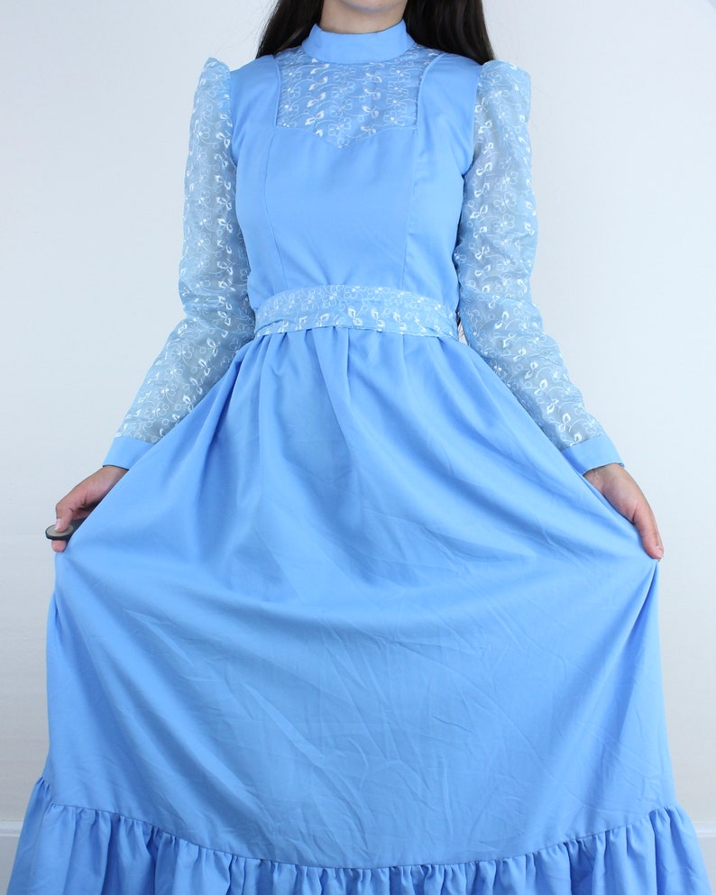 May include: A light blue maxi dress with long sleeves and a white lace overlay. The dress has a high neck and a fitted bodice with a gathered skirt.