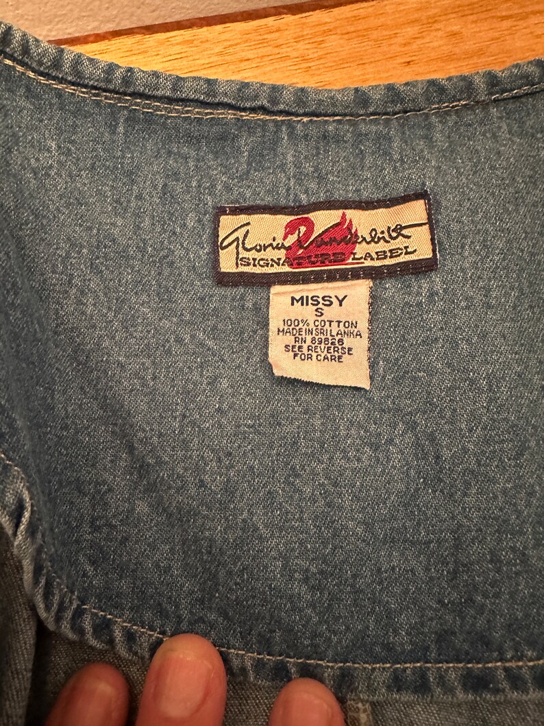 May include: A blue denim vest with a brown label that reads "Gloria Vanderbilt Signature Label" and a white tag that reads "Missy S 100% Cotton Made in Sri Lanka RN 89826 See Reverse for Care".
