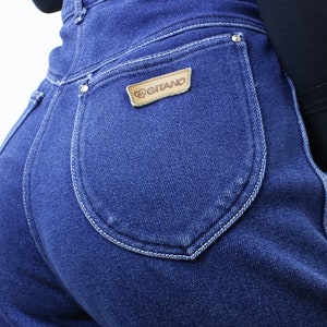 May include: A pair of blue denim jeans with a back pocket featuring a brown leather patch with the text "Gitano" in white.