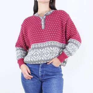 May include: A pink and gray patterned sweater with a button-up collar. The sweater has a snowflake design on the bottom half.