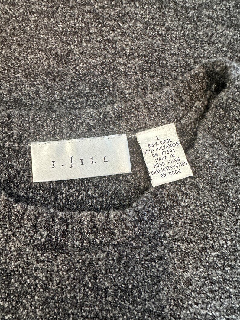 May include: A gray J.JILL sweater tag with the text "J.JILL" and size "L" with the fabric content: 83% wool, 17% polyamide, RN 97641, Made in Hong Kong, Care Instruction on Back.