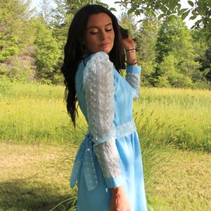 May include: A light blue dress with a white lace overlay on the sleeves. The dress has a cinched waist and a flowing skirt.
