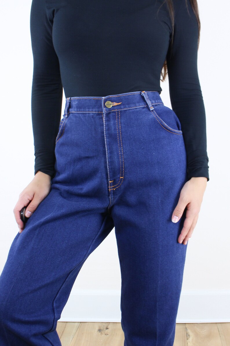 May include: A pair of high-waisted blue denim jeans with a button fly and orange stitching.