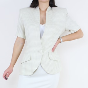May include: A white blazer with a checkered pattern and short sleeves. The blazer has a single button closure and two pockets.