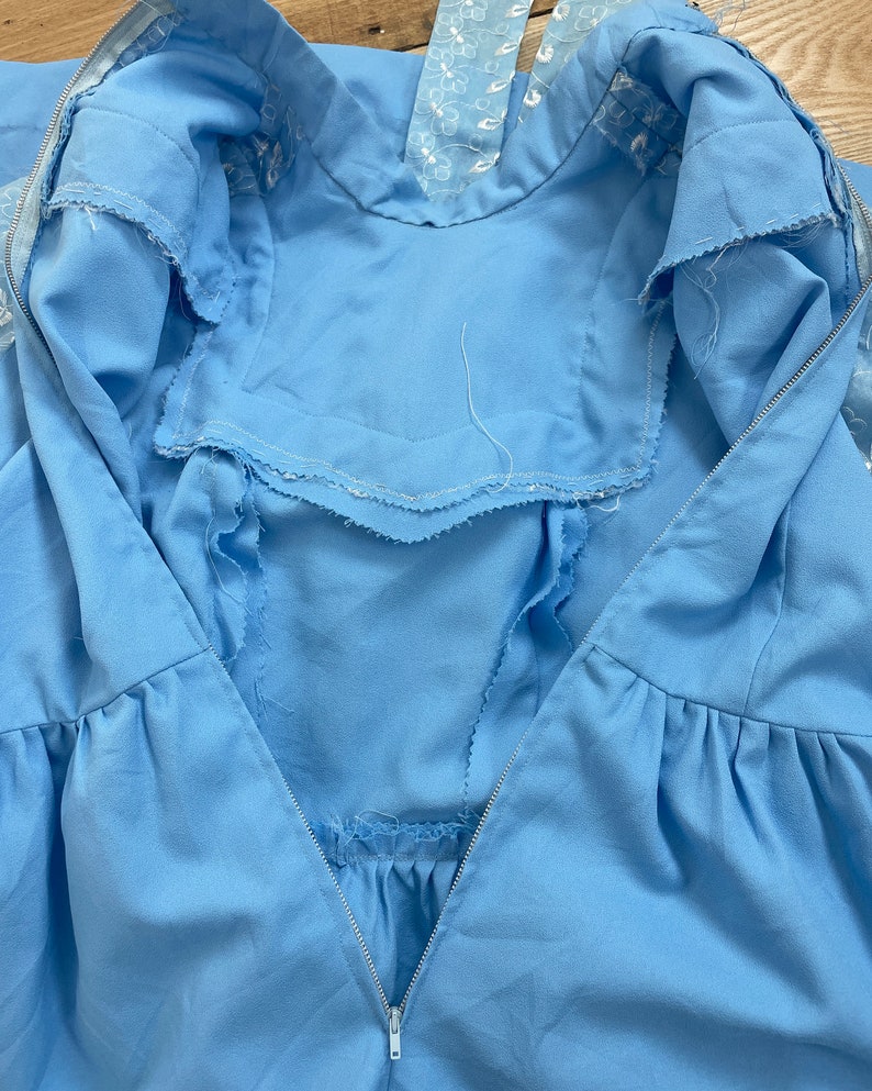 May include: A light blue dress with a zipper closure and a white embroidered neckline.