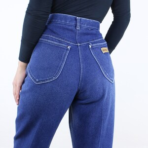 May include: A pair of high-waisted blue denim jeans with a back pocket featuring a brown leather patch with the word "Wrangler" on it.
