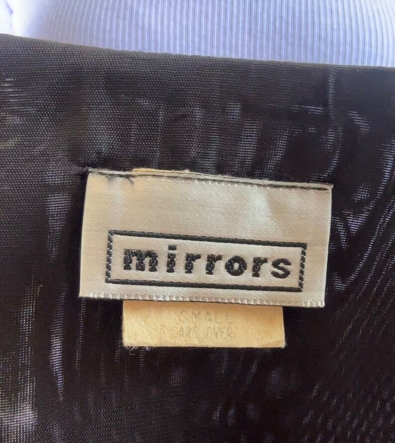 May include: A white tag with black text that reads "mirrors" on a black fabric background. The tag also has a smaller white tag that reads "Small Size Over".