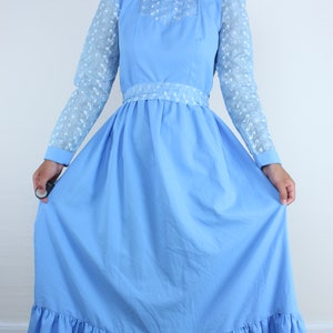 May include: A light blue maxi dress with a high neck and long sleeves. The sleeves are made of a sheer lace fabric with a floral pattern. The dress has a fitted bodice and a full skirt with a ruffle trim.