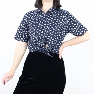 May include: A navy blue short-sleeved shirt with a white paisley print. The shirt is tied at the waist and is worn with a black velvet skirt.