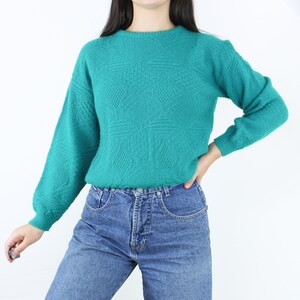 May include: A teal blue knitted sweater with a geometric pattern. The sweater has long sleeves and a round neckline.
