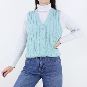 May include: A light blue cable knit vest with a button closure. The vest has two pockets on the front.