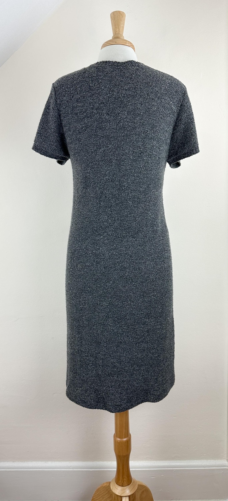 May include: A gray short-sleeved dress with a textured knit fabric. The dress is on a wooden mannequin.