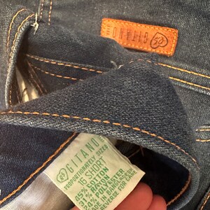 May include: A green and white clothing label with the text "Gitano" and "16 Short" and the fabric content: 45% Cotton, 31% Rayon, 20% Polyester. The label also states "Proportionately Sized" and "Made in Bangladesh".