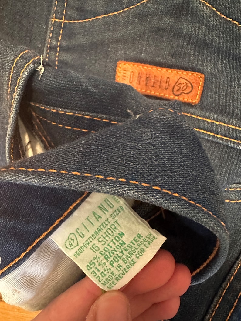 May include: A green and white clothing label with the text "Gitano" and "16 Short" and the fabric content: 45% Cotton, 31% Rayon, 20% Polyester. The label also states "Proportionately Sized" and "Made in Bangladesh".